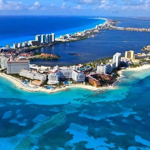 Aerial view of Cancun, Mexico, a coastal city with high-rise buildings and a mix of sandy beaches and turquoise waters. The city extends along the shoreline, blending urban structures with natural elements. The ocean showcases various shades of blue and green, epitomizing vibrant coastal beauty.