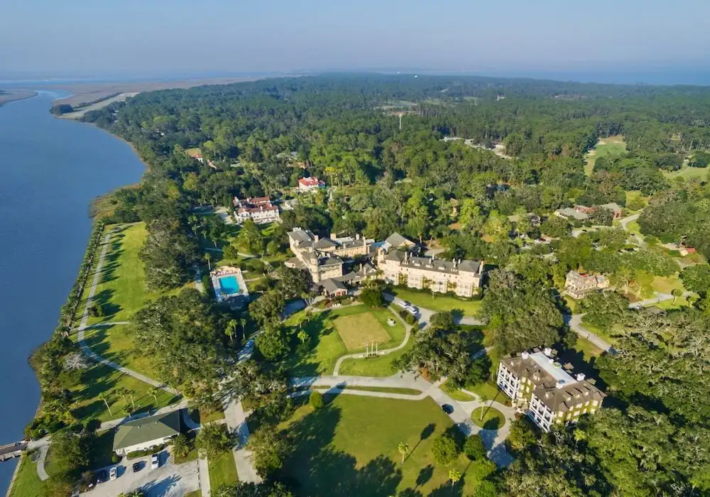 Aerial view of a large estate with historic buildings, lush greenery, and a river on the left, reminiscent of Jekyll Island's scenic charm, best kept-secret vacation spots east coast